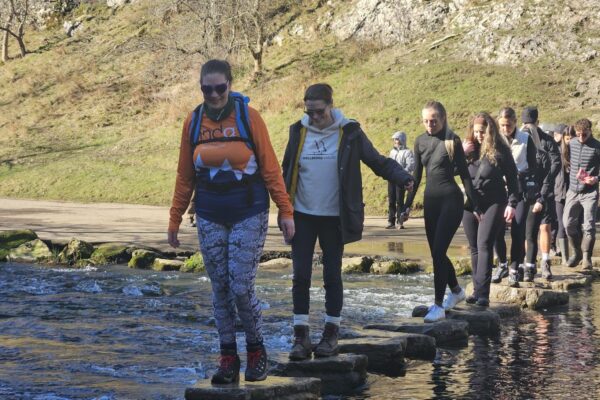 Group walking over the stepping stones in Dovedail , peak district Corporate wellbeing event