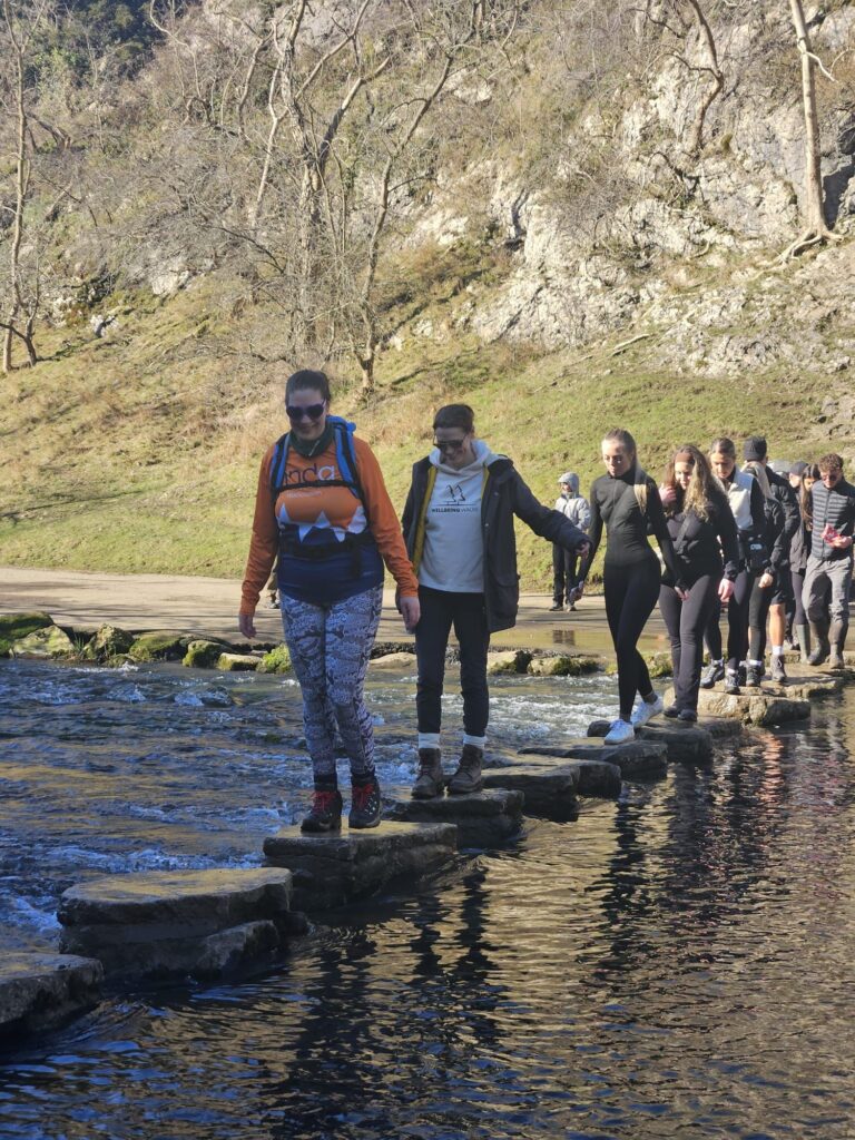 Group walking over the stepping stones in Dovedail , peak district Corporate wellbeing event