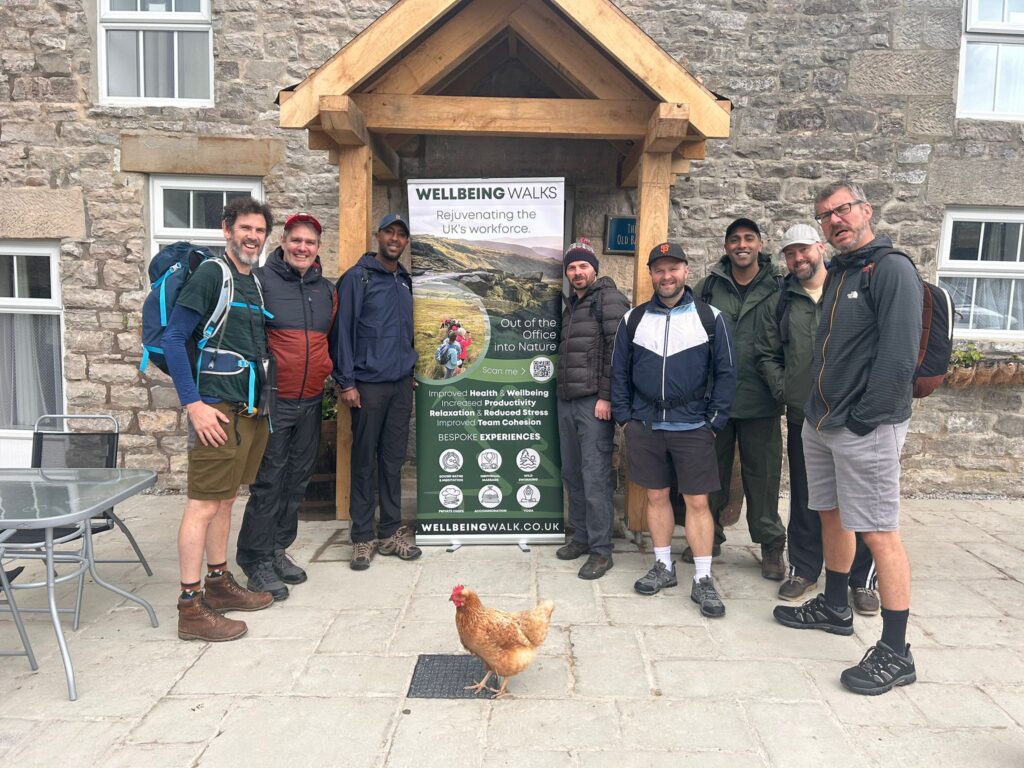 Group stood outside a cottage with a chicken in the picture and a wellbeing walks banner