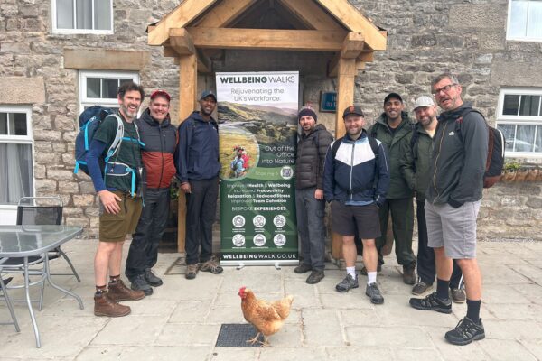 Group stood outside a cottage with a chicken in the picture and a wellbeing walks banner